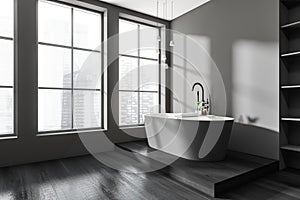 Dark bathroom interior with bathtub, panoramic window with city view, shelf niche, grey walls, hardwood floor. Concept of hygienic