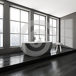 Dark bathroom interior with bathtub, panoramic window with city view, shelf niche, grey walls, hardwood floor. Concept of hygienic
