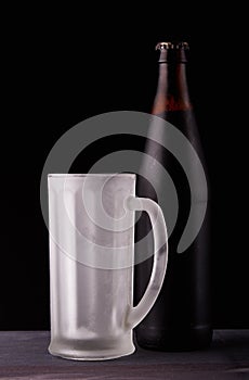 Dark beer in bottle and empty frost-coated mug.