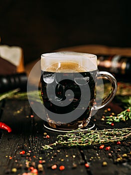 Dark beer with foam in a mug on the wooden background