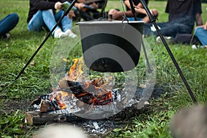 Dark big pot or cauldron, cooking pan with boiling water inside above the fire somewhere in the park or mountains