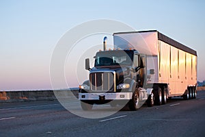 Dark big rig semi truck with bulk trailer running on highway in