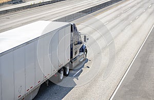 Dark big rig semi truck transporting cargo in dry van semi trailer running on wide multiline highway road