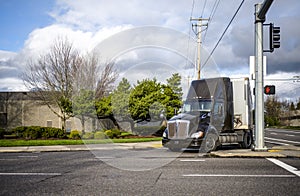 Dark big rig semi truck turning on the city crossroad intersection