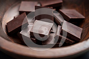 Dark bitter chocolate pieces in wooden brown rustic bowl. Food pleasure concept