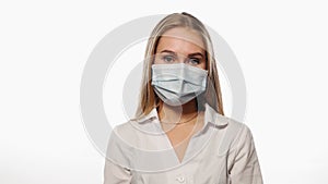Dark blond haired nurse in a medical mask shows indifference or disinterest or apathy with her face, looks at the camera