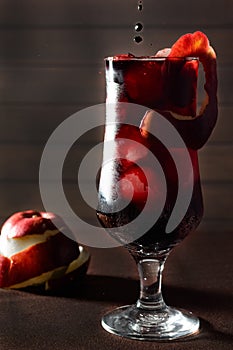 A dark blood cocktail with ice and a red apple, in a tall glass, on a dark background, a symbol of bloodshed in the war, death