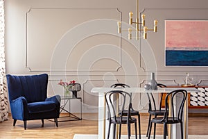 Dark blue armchair in a dining room interior with a table, chairs and golden lamp