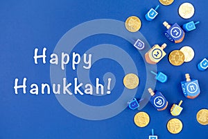 Dark blue background with dreidels and chocolate coins and Happy Hanukkah wording. Hanukkah and judaic holiday concept.