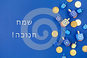 Dark blue background with multicolor dreidels and chocolate coins and Happy Hanukkah wording in Hebrew