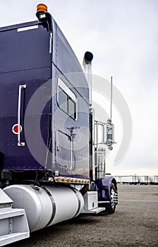Dark blue big rig classic semi truck tractor with aluminum accessories standing on the parking lot waiting for load for next