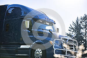 Dark blue big rig semi truck tractor with pipe grille guard running on the road at sunshine