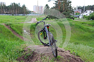 The dark blue bike stands on a hill against a background of green grass and beautiful scenery.