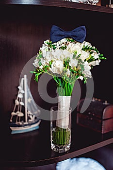 Dark blue bow tie on a luxury bridal bouquet of white flowers on a shelf