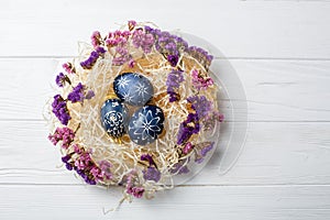 Dark blue easter eggs in nest on white wooden background
