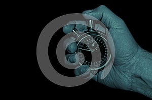 dark blue image of hand holding a mechanical stopwatch on black background