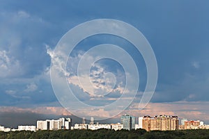 Dark blue rainy clouds in sunset sky over city