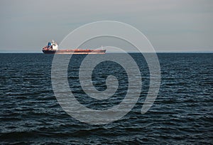 A dark blue sea and a large red-black dry cargo ship on the horizon