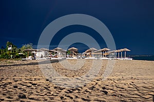 The dark blue sky is above the beach bar by the sea. It`s like a storm. The beach is empty and there are no people