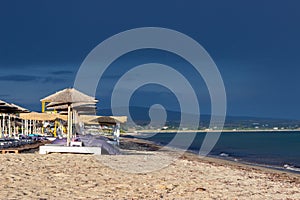 The dark blue sky is above the beach by the sea. It`s like a storm. The beach is empty and there are no people