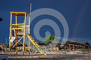 The dark blue sky is above the beach by the sea. It was as if there was a storm, and it turned out to be a rainbow. The beach is