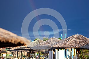 The dark blue sky is above the beach by the sea. It was as if there was a storm, and it turned out to be a rainbow. The beach is