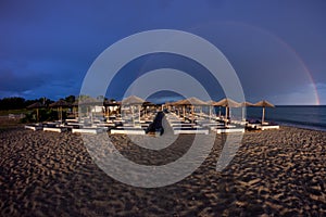 The dark blue sky is above the beach by the sea. It was as if there was a storm, and it turned out to be a rainbow. The beach is