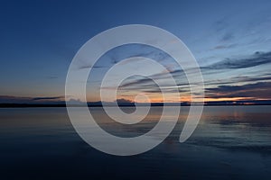 Dark blue sky in the twilight glow of sunset is reflected in the quiet surface of the water of the lake