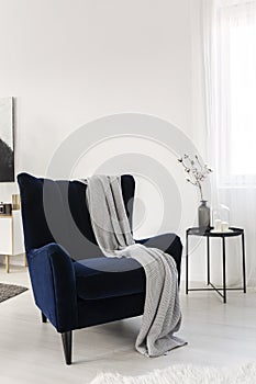 Dark blue velvet wing back chair with grey blanket in trendy living room