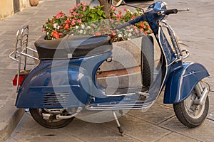 Dark blue vintage Vespa  against a background of brighly coloured flowers