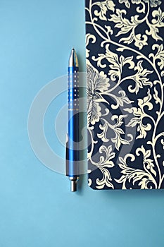 Dark blue and white floral notebook with blue pencils on white and blue background, detail