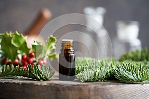 A dark bottle of essential oil with fir and holly branches