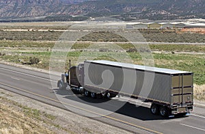 Dark brown classic American big rig semi truck transporting aluminum refrigerated semi trailer on the road in Utah