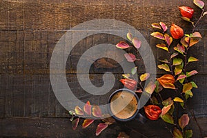 Dark brown clay cup with black coffee and branches of autumn leaves Spiraea Vanhouttei with Physalis on the old wooden table. To