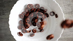 Dark brown cornflakes in form of chocolate-flavored breakfast circles are showered on plate close-up