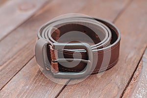 Dark brown men`s belt with buckley on a wooden desk