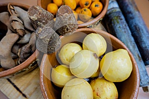 Dark brown sugar canes between clay bowls of fruit
