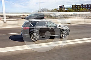 Dark brown SUV car driving fast on a highway with motion blur effect