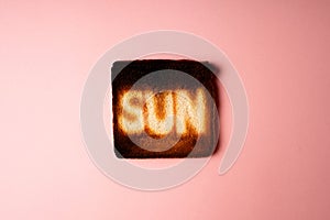 dark burnt slices of white bread toast with the word Sun on it on pink background.
