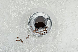 A dark ceramic cup with expresso on a plaster tray with coffee beans stands on a gray concrete table. top view. a copy of the
