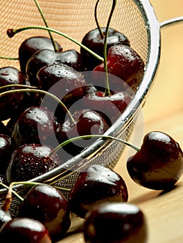 Dark cherries in mesh sieve on wooden table