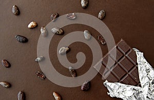 Dark chocolate bar in foil wrapper and cocoa beans