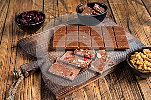 Dark chocolate bar with hazelnuts, peanuts, cranberries and freeze dried raspberries on a wooden board. wooden