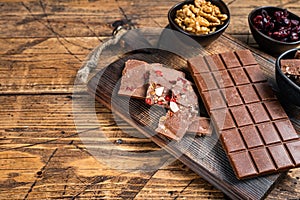 Dark chocolate bar with hazelnuts, peanuts, cranberries and freeze dried raspberries on a wooden board. wooden