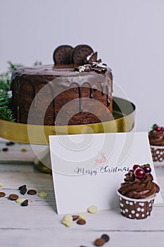 Dark chocolate cake with cookies and cupcakes berries on white wooden background. Lettering. Postcard