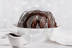 Dark chocolate cake covered with icing on a white stand. Selective focus.