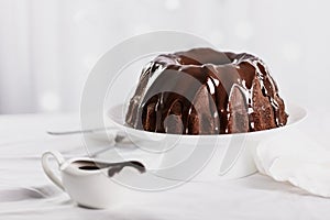 Dark chocolate cake covered with icing on a white stand. Selective focus.