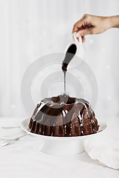 Dark chocolate cake covered with icing on a white stand. Selective focus.