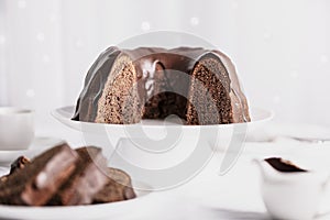 Dark chocolate cake covered with icing on a white stand. Selective focus.