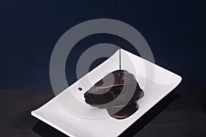 Dark chocolate with chocolate pouring isolated over dark reflective surface